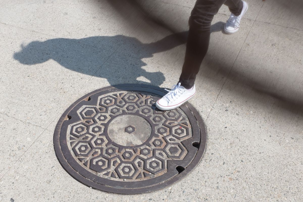 Kanaldeckel über den jemand läuft, von dem man nur Jeans und Turnschuhe sieht