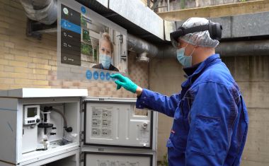 Mitarbeiter mit der Hololensbrille steht vor dem Probenahmeschrank . Er tippt auf einen  Bildschirm, dass die Hololens vor seinem Gesicht  projiziert