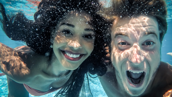 junges Paar lacht in die Kamera unter Wasser im Pool