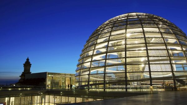 Die beleuchtete Glaskuppel des Reichstags in Berlin in der Dämmerung.