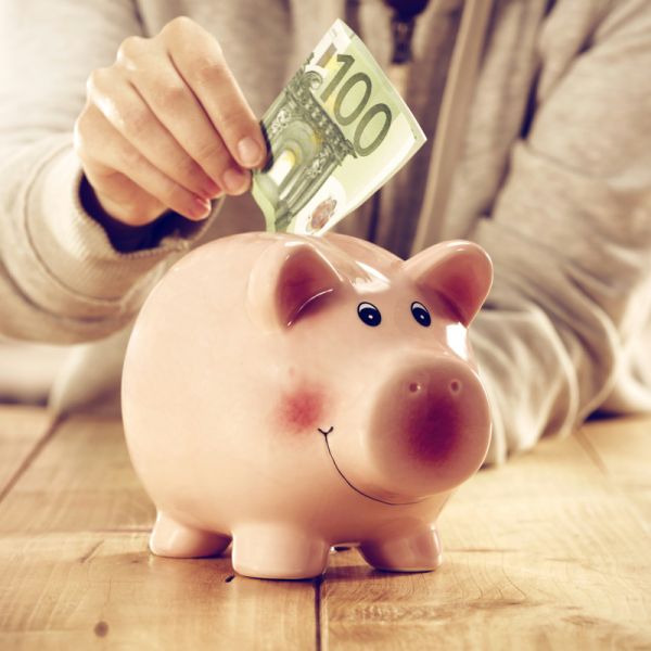 Eine Hand steckt einen 100 Euro Schein in ein Sparschwein
