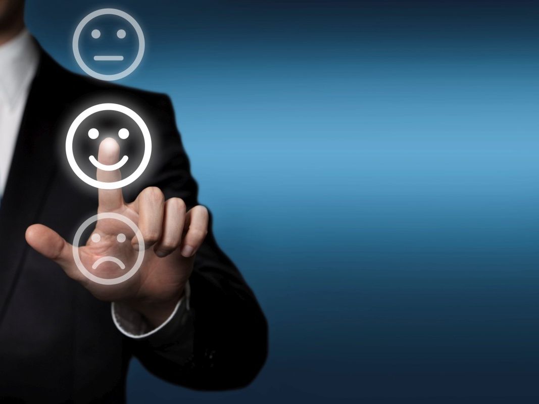 Geschäftsmann steht an einer transparenten Touchscreen-Fläche. Er berührt mit seinem Zeigefinger das mittlere, lächelnde, der 3 Smile-Symbole.