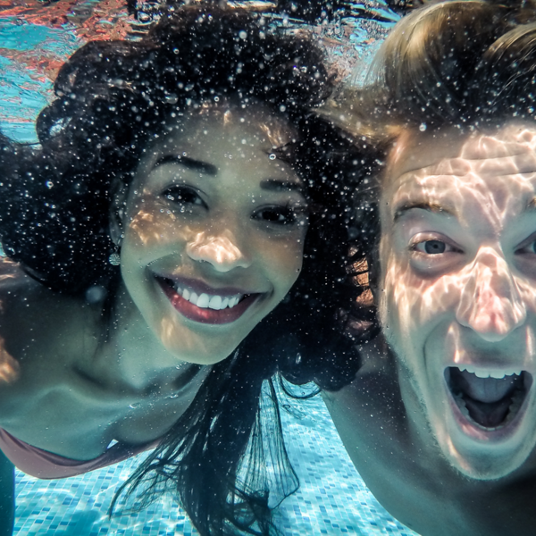 junges Paar lacht in die Kamera unter Wasser im Pool