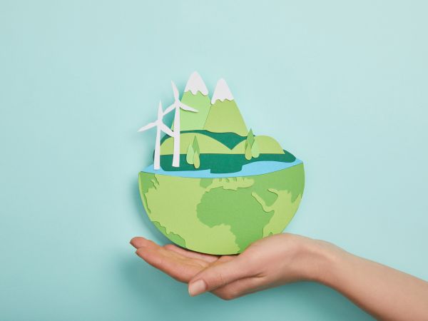 Planet aus Papier mit erneuerbaren Energien gehalten von einer Hand