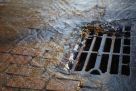 Abwasser läuft in einen vergitterterten Einlaufschacht für Strassenabwässer am Rand einer gepflasterten Straße.
