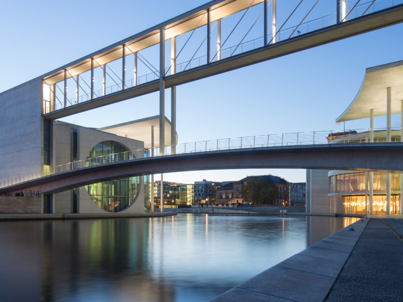 Moderne Regierungsgebäude an einem Fluss in der Abenddämmerung, verbunden durch beleuchtete Fußgängerbrücken.