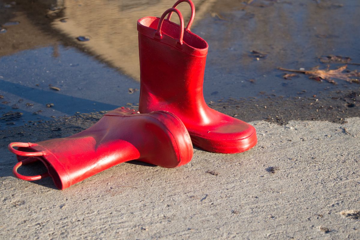 ein liegender und ein stehender Gummistiefel in einem leuchtenden Rot vor einer Pfütze