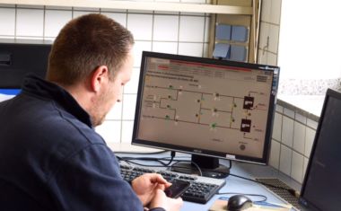 Mitarbeiter sitzt vor dem PC und tippt auf sein Handy