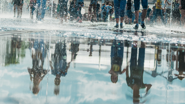 Spiegelung der Menge fröhlicher Menschen beim Stadtbrunnen. Heller, sonniger Frühlings- oder Sommertag