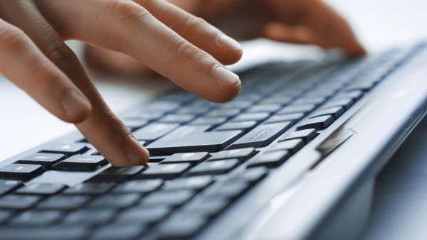 Eine Person bedient zweihändig eine Computertastatur, wobei die linke Hand und der größte Teil der Tastatur undeutlich zu sehen ist und die rechte Hand im Vordergrund deutlich.