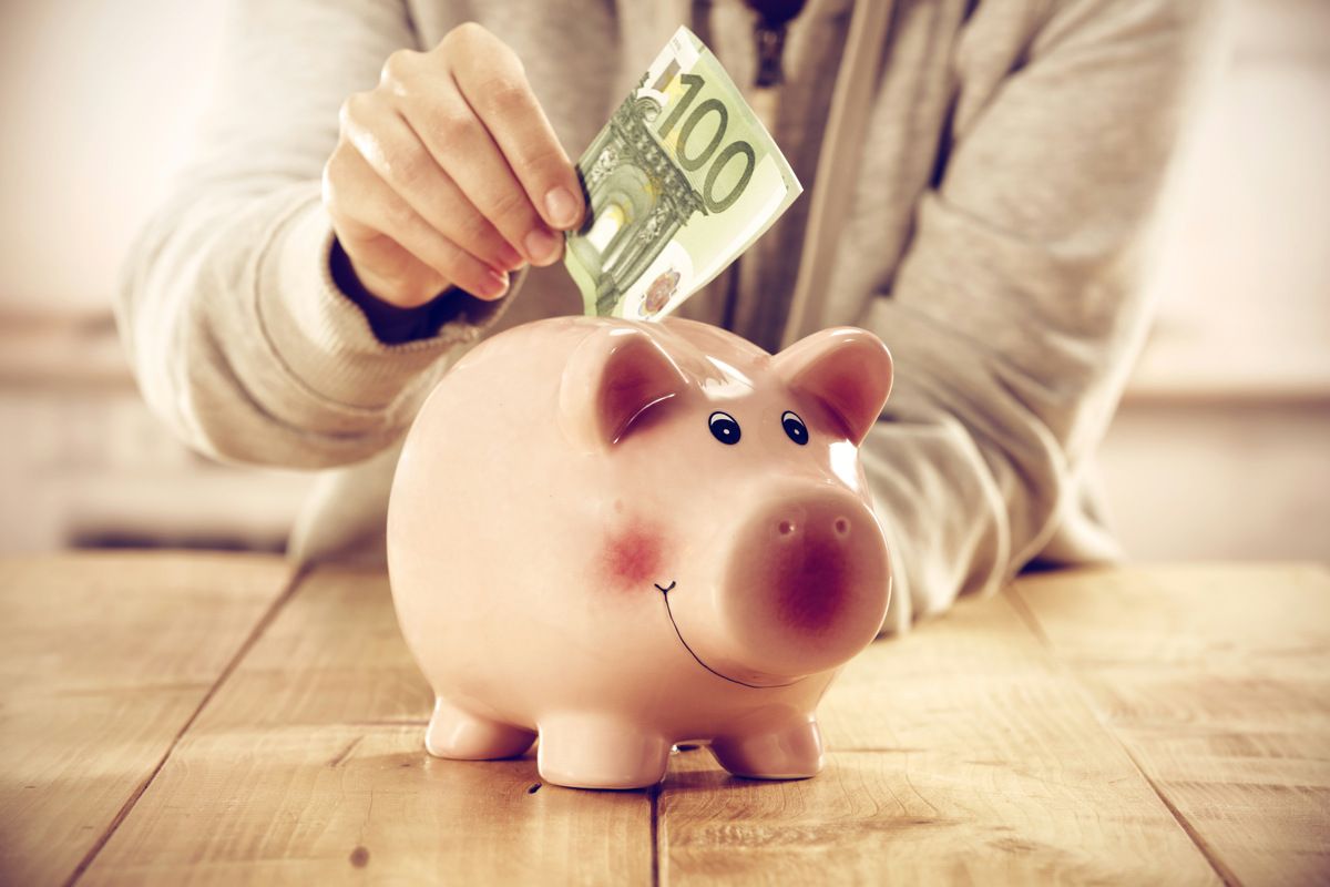 Eine Hand steckt einen 100 Euro Schein in ein Sparschwein
