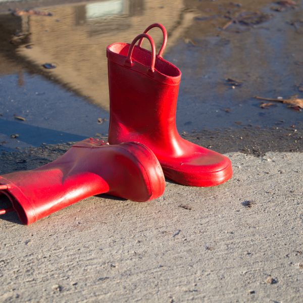 ein liegender und ein stehender Gummistiefel in einem leuchtenden Rot vor einer Pfütze