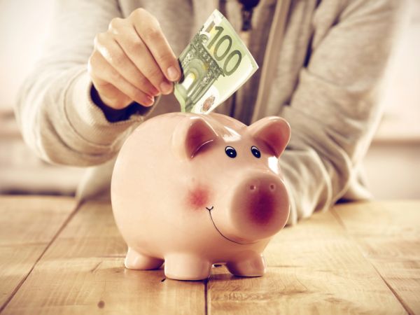 Eine Hand steckt einen 100 Euro Schein in ein Sparschwein