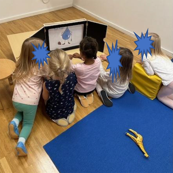 Kinder sitzen vor einem Kamishibai-Theater und schauen auf die Karte von Trulli Tropf