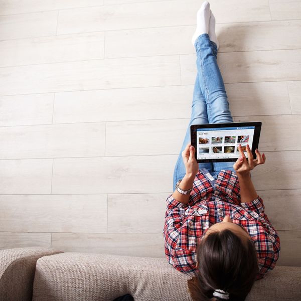 Fot von oben auf eine junge Frau, die sich an eine Couch anlehnt und auf einem Tablet liest